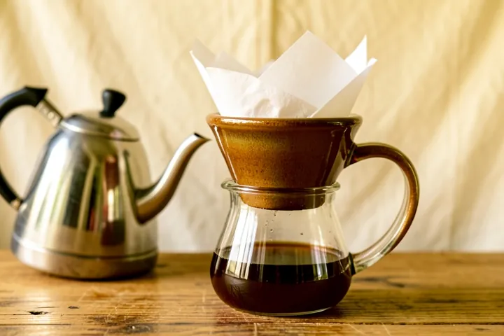 A ceramic pour-over dripper on a glass carafe of coffee, beside a steel kettle
