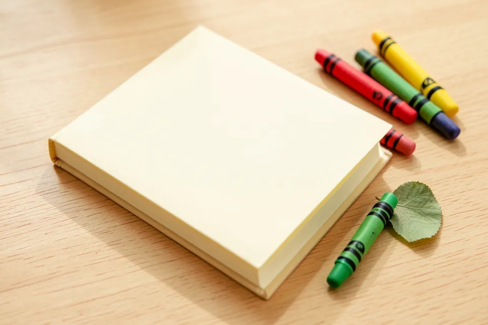 A small diary with crayons and a pressed leaf on a wooden table